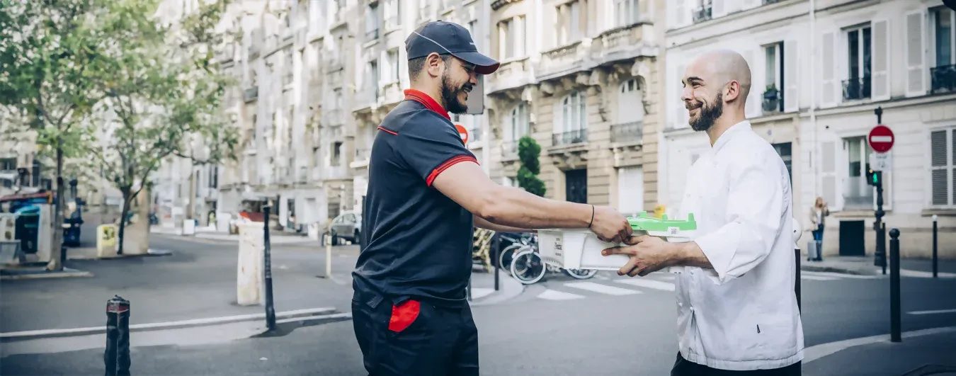 Un chauffeur-livreur Transgourmet remet une caisse de poissons frais Pandobac à un chef cuisinier devant son restaurant.