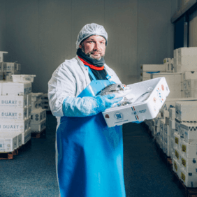 Alexandre, responsable de production chez Transgourmet Seafood avec une cagette de poissons entier dans les bras, dans un atelier de Transgourmet Seafood.